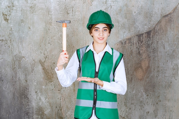 Travailleur de la construction féminin en casque vert posant avec un marteau