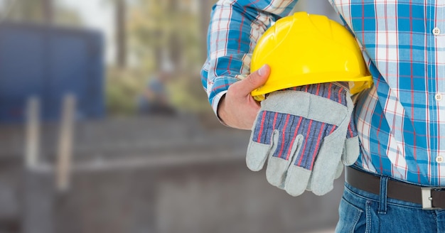 Travailleur de la construction avec des gants de sécurité et un chapeau devant le chantier de construction