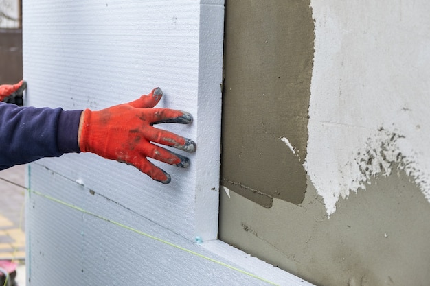 Photo travailleur de la construction installant des feuilles d'isolation en polystyrène sur le mur de la façade de la maison pour la protection thermique.