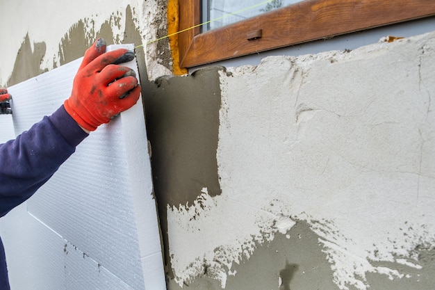 Travailleur de la construction installant des feuilles d'isolation en polystyrène sur le mur de la façade de la maison pour la protection thermique.