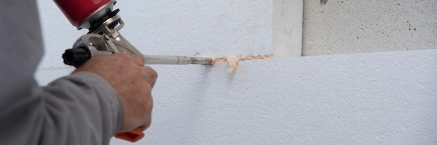 Photo travailleur de la construction installant des feuilles d'isolation en polystyrène et remplissant l'espace entre avec l'expansion