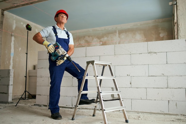 Travailleur de la construction professionnel en uniforme debout avec perceuse à percussion rotative portrait de l'entrepreneur