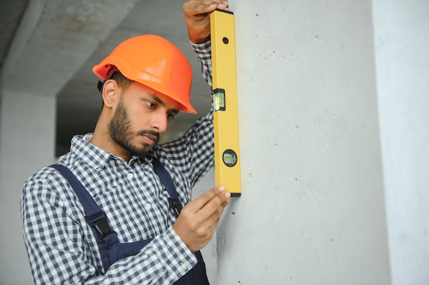 Travailleur de la construction de sexe masculin indien debout en uniforme et casque sur le chantier de construction