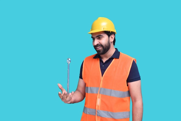 Travailleur de la construction souriant portant un gilet réfléchissant et tenant une clé modèle pakistanais indien