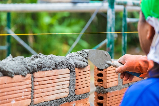 Photo travailleur de la construction utilisant une truelle pour ajouter du mortier de ciment sur le mur de briques
