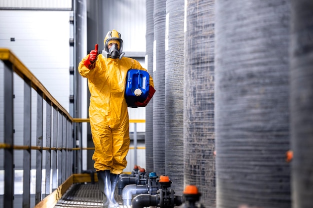 travailleur en costume de protection masque à gaz et gants debout près de réservoirs métalliques avec de l'acide dans une usine de produits chimiques