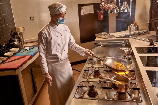 Travailleur de cuisine asiatique faisant frire des légumes sur une grande flamme