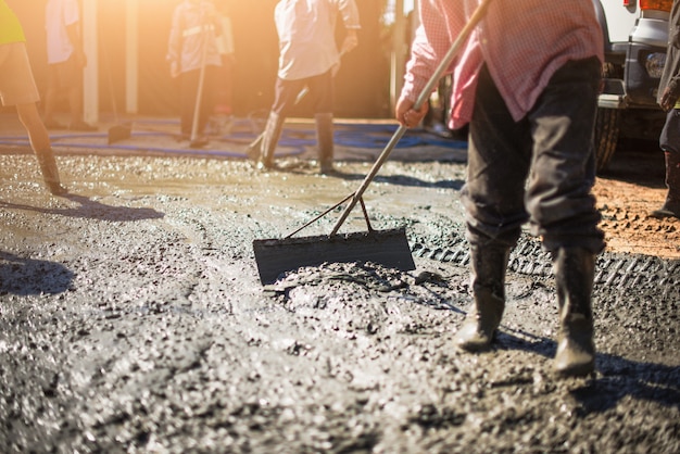 Travailleur dans des bottes en caoutchouc se dresse dans du ciment non encombré et nivelle la surface