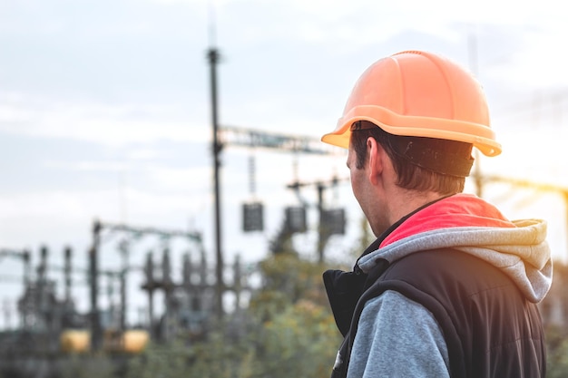 Travailleur dans un casque dans le contexte d'une sous-station et de poteaux à haute tension