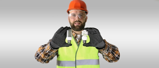 Photo travailleur dans un casque et des vêtements de protection avec une ampoule dans les mains