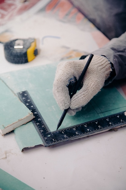 Un travailleur dans un gant avec un crayon noir annule les dimensions sur la planche selon la règle