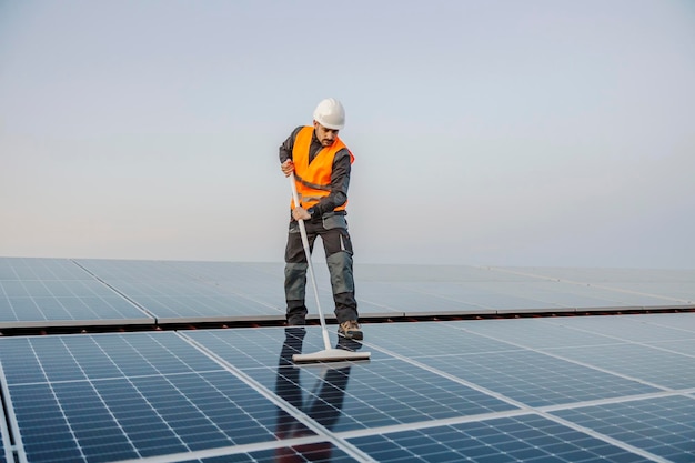 Un travailleur debout sur le toit et nettoyant les panneaux solaires de la saleté