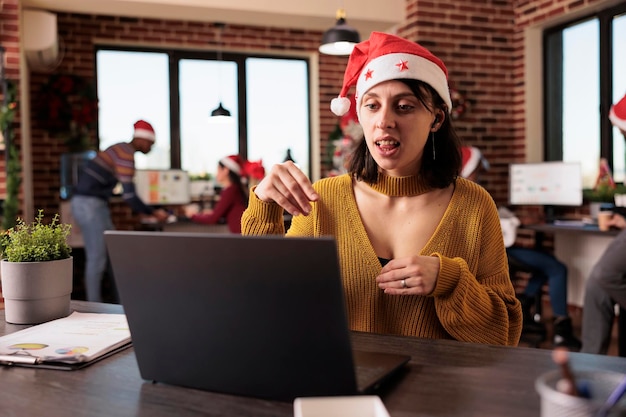 Travailleur de démarrage discutant lors d'une réunion par vidéoconférence au travail, parlant lors d'un appel de vidéoconférence à distance au bureau avec un arbre de noël. Femme utilisant le chat par téléconférence dans un lieu de travail festif.