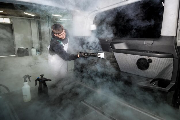 Travailleur détaillant l'intérieur de la voiture de nettoyage avec un nettoyeur à vapeur