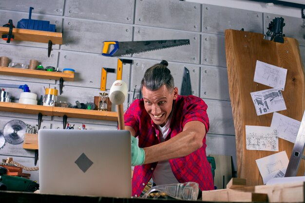 Un travailleur énervé dans l'atelier bat un ordinateur portable avec un marteau