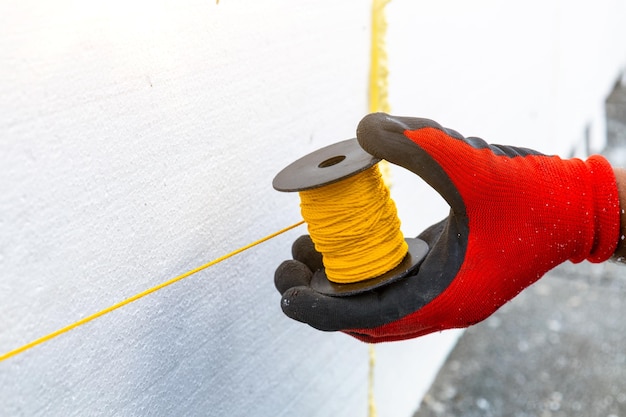 Le travailleur enroule la corde Doityourself en collant des feuilles d'isolation en mousse à la maison