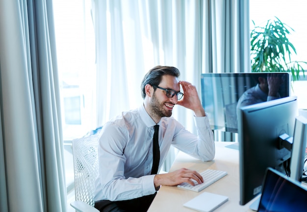 Travailleur d'entreprise souriant en tenue de soirée à l'aide d'un ordinateur de bureau et assis dans son bureau.