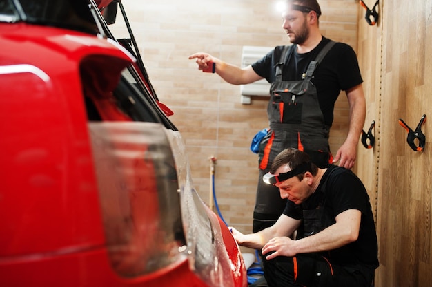 Le travailleur de l'entretien automobile a mis un film anti-gravier sur une carrosserie de voiture rouge à l'atelier de détail du véhicule Protection de la voiture avec des films spéciaux