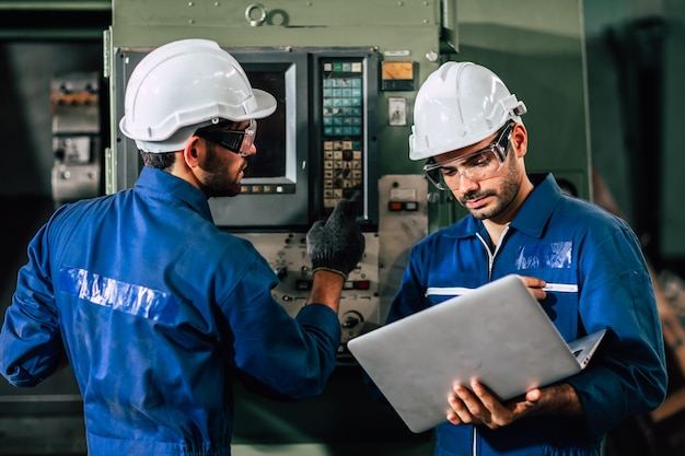 Le travailleur de l'équipe d'ingénieur de l'industrie utilise une machine lourde de contrôle avec un ordinateur portable pour aider à analyser le problème de fonctionnement.