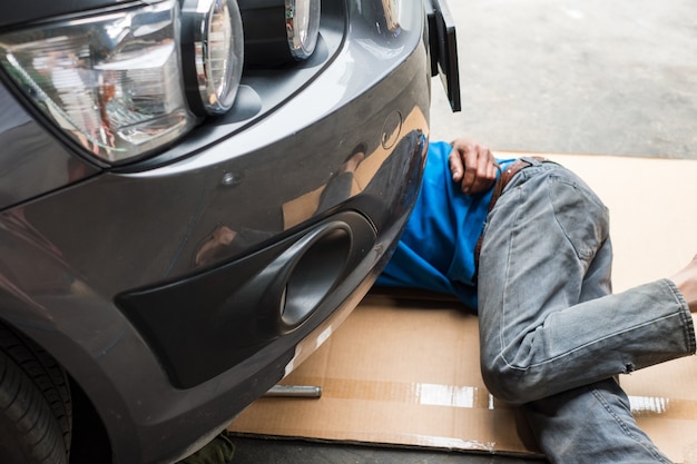 Le travailleur est sous la voiture pour changer l'huile moteur