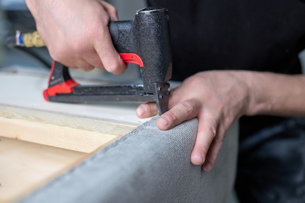 Le travailleur fixe le tissu avec une agrafeuse pneumatique dans le magasin d'usine