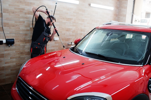 Travailleur homme lave voiture rouge dans garage détaillant