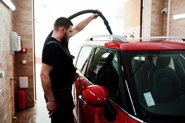 Travailleur homme séchant une voiture rouge dans un garage détaillant après le lavage