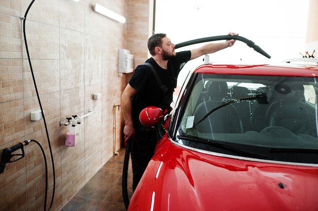 Travailleur homme séchant une voiture rouge dans un garage détaillant après le lavage