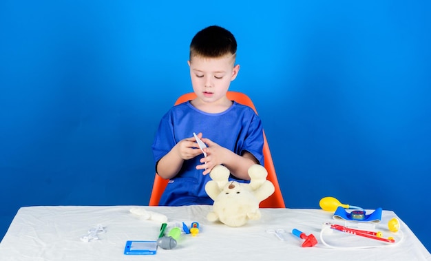 Travailleur hospitalier Soins de santé Enfant petit médecin occupé assis à table avec des outils médicaux Examen médical Concept de médecine Procédures médicales pour ours en peluche Garçon enfant mignon future carrière de médecin