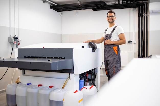 Un travailleur d'impression souriant utilise un ordinateur pour plaquer une machine dans une imprimerie.