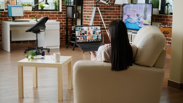 Travailleur Indépendant Travaillant à Domicile Tout En Discutant Avec Des Collègues Lors D'une Conférence Internet. Femme Travaillant à Distance Depuis Son Domicile Lors D'un Appel Vidéo De Réunion En Ligne Sur Un Ordinateur Portable Assis Dans Le Salon.