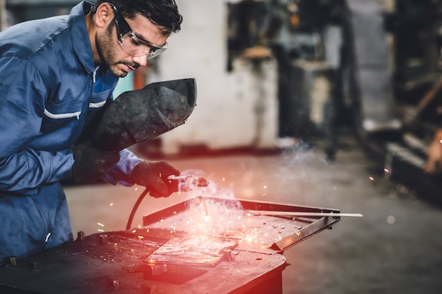 Travailleur de l'industrie en acier de soudage tig avec masque de sécurité pour protéger la vue dans l'usine de métal.