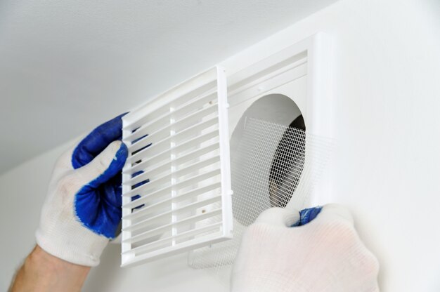 Le travailleur installe une grille de ventilation.