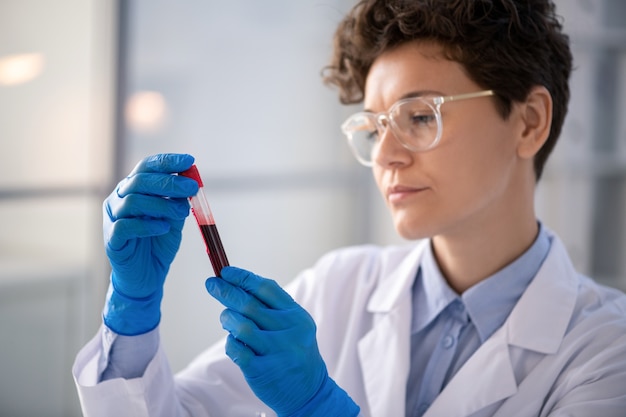 Travailleur de laboratoire occupé dans des gants en latex analysant la couleur de l'échantillon de sang d'un patient atteint de coronavirus dans un tube à essai