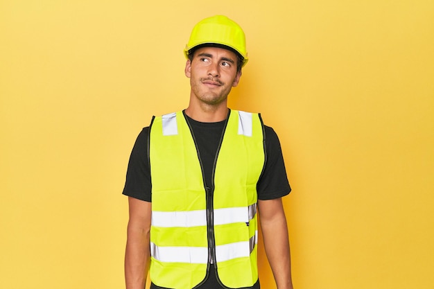 Photo travailleur latino en gilet jaune et casque rêvant d'atteindre ses buts et ses objectifs