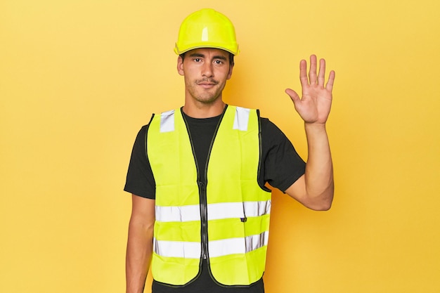 Photo travailleur latino en gilet jaune et casque souriant joyeux montrant le numéro cinq avec les doigts