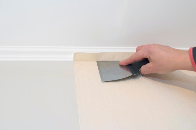 Le travailleur lisse le papier peint avec une spatule sur le mur pendant le concept de réparation de réparation