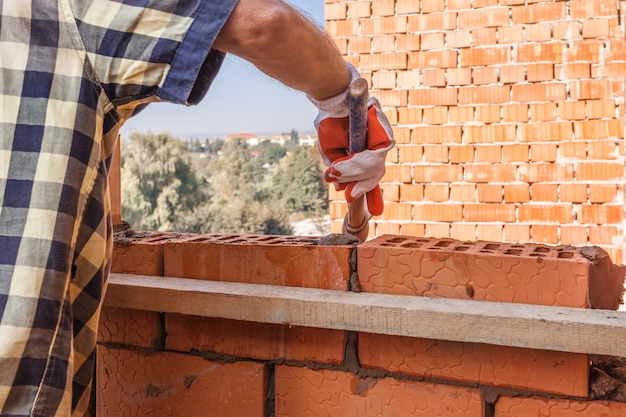 Travailleur de maçon installant la maçonnerie de brique sur le mur extérieur avec la truelle