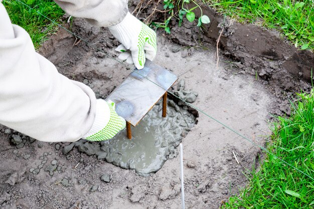 Le travailleur mans les mains dans les gants martelent la construction en fer dans une solution de ciment, du lisier, du mortier de béton. Préparation du processus de construction, rénovation, pose des fondations de la maison.