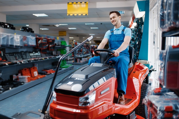 Travailleur masculin assis sur une tondeuse à gazon dans un magasin d'outils