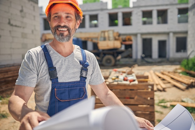 Travailleur masculin caucasien gai et mûr avec des plans regardant au loin