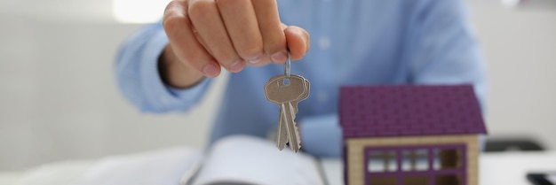 Un travailleur masculin en costume donne la clé pour déverrouiller une nouvelle maison miniature acheter un nouveau logement