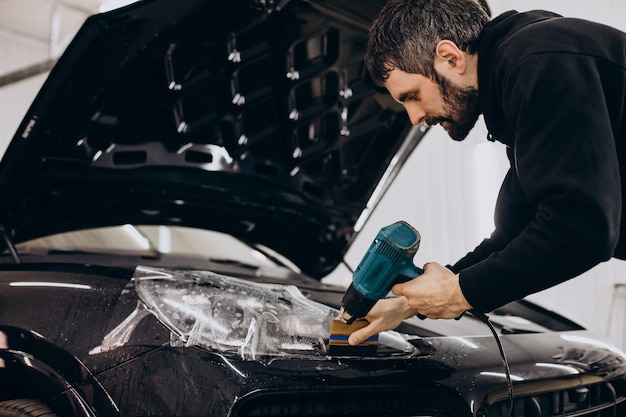 Travailleur masculin enveloppant une voiture avec une feuille de protection