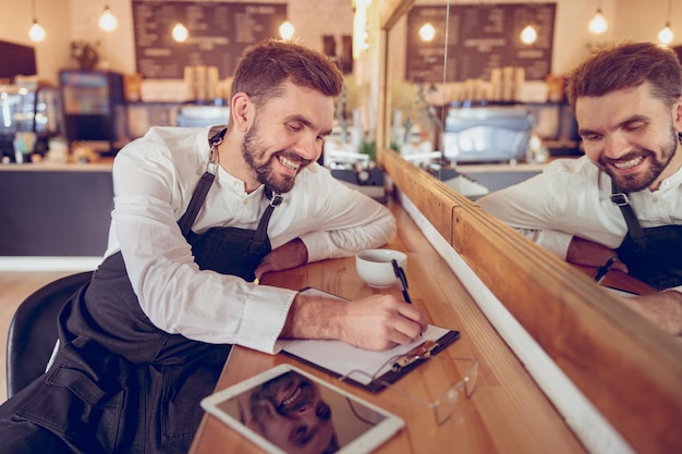 Travailleur masculin gai écrivant sur le presse-papiers dans le café