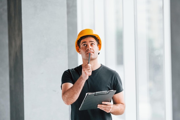 Travailleur masculin ou ingénieur en casque jaune debout à l'intérieur avec bloc-notes