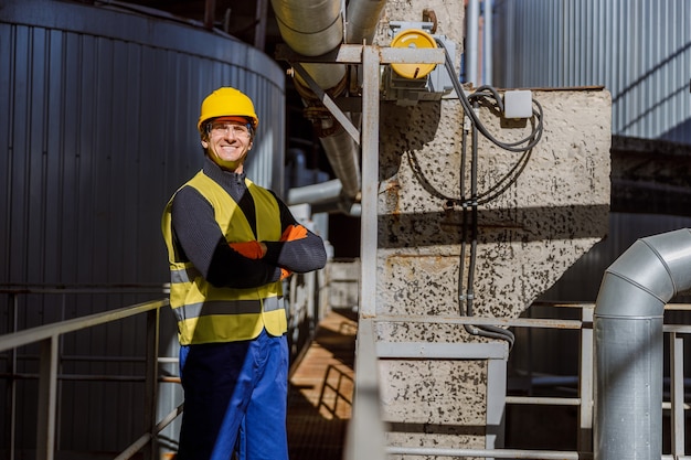 Travailleur masculin joyeux se tenant sur le pont en métal à l'usine