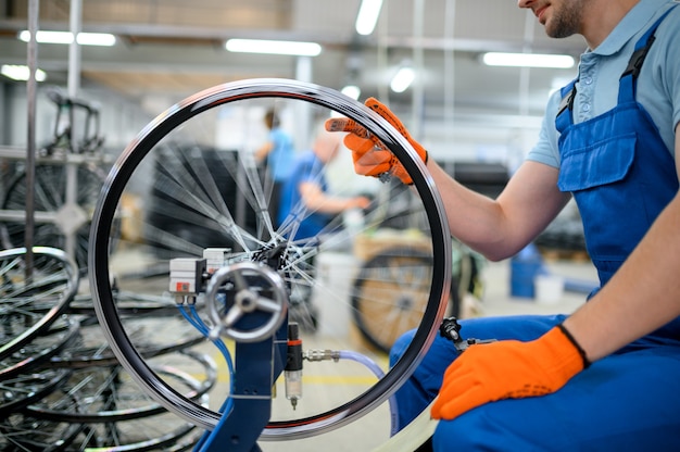 Travailleur masculin à la machine-outil vérifie la jante de bicyclette en usine. Montage de roues de vélo en atelier, installation de pièces de vélo