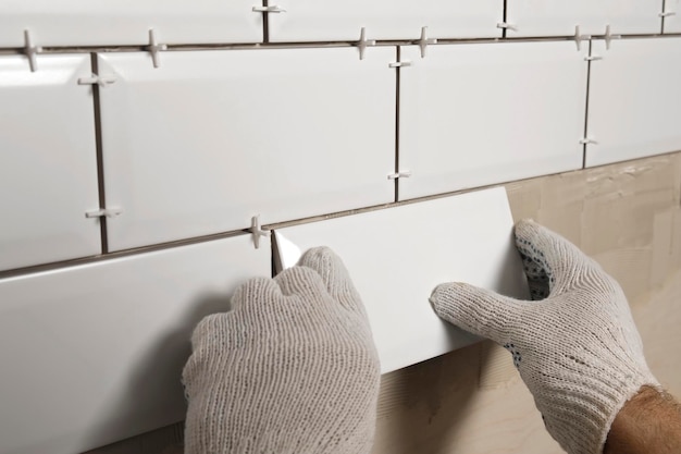 Travailleur masculin maître pose des carreaux de céramique sur le mur de la cuisine réparateur plaçant des carreaux modernes blancs épandant de l'adhésif constructeur installant des carreaux à la réparation des travaux de rénovation carrelage professionnel