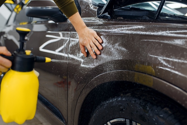 Un travailleur masculin mouille la surface de l'aile de la voiture avec un spray avant d'appliquer le film de protection. Installation de revêtement qui protège la peinture de l'automobile des rayures. Nouveau véhicule dans le garage, détaillant