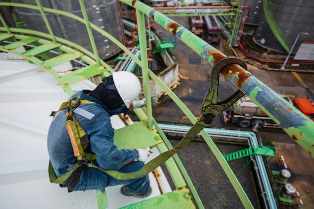Travailleur masculin portant un harnais de sécurité d'abord et un seul de sécurité travaillant à un endroit élevé de la main courante sur le produit chimique du réservoir de toit supérieur.